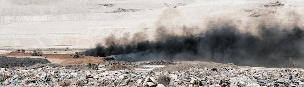 Panorama of black smoke over burning old tyres and piles of garbage at landfill sitexA