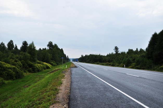 Panorama of a deserted road. Thunderclouds before the rain. Green trees along the road.