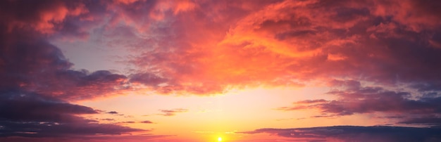 Panorama of dramatic colorful sunset with dark and bright clouds. The sun's rays are breaking through the cloudy sky. Dark clouds against a bright saturated sky.