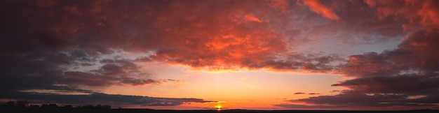 Panorama of dramatic colorful sunset with dark and bright clouds. The sun's rays are breaking through the cloudy sky. Dark clouds against a bright saturated sky.