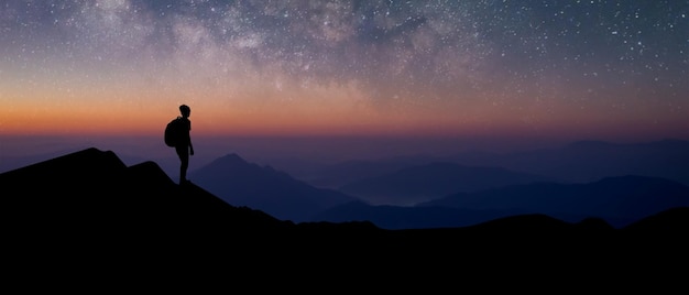 Panorama silhouette of young traveler with backpack standing and watched the star and milky way alone on top of the mountain He enjoyed traveling and was successful when he reached the summit