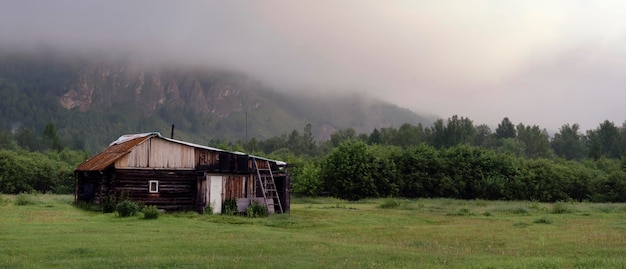 Panorama of a simple rural lonely house in the morning forest at the foot of the hills near the fore