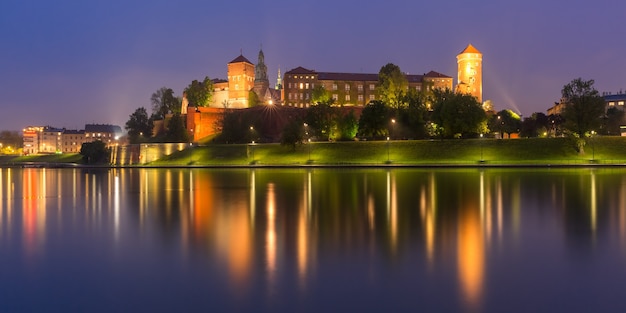 Panorama of Wawel Castle on Wawel Hill with reflection in the river at night as seen from the Vistula, Krakow, Poland