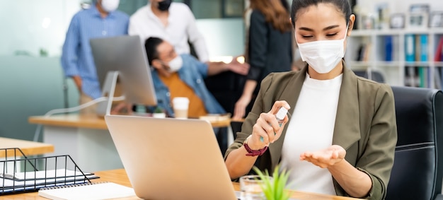 Panoramic Asian office employee businesswoman wear face mask use alcohol spray hand sanitizer