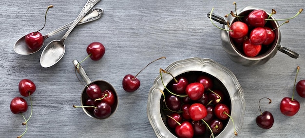 Panoramic banner cherry in vintage metal plate with spoons Panorama image flat lay top view on grey wooden background