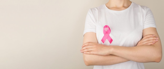 Panoramic photo of woman with crossed arms in white tshirt with pink ribbon symbol of breast cancer awareness on isolated grey background