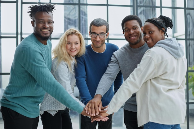 Panoramic shot of cheerful businesswomen and multicultural men putting hands together