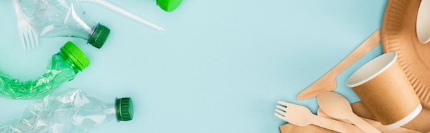 Panoramic shot of disposable tableware and wooden cutlery near crumpled plastic bottles on blue