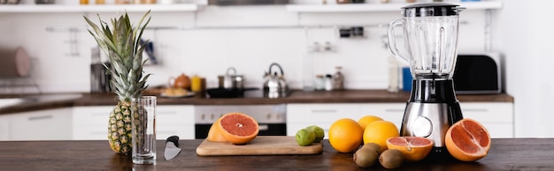 Panoramic shot of fresh fruits near blender on table in kitchen