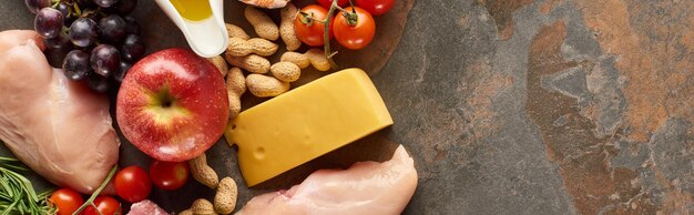 Photo panoramic shot of raw poultry fillet with fruits peanuts tomatoes cheese on marble surface