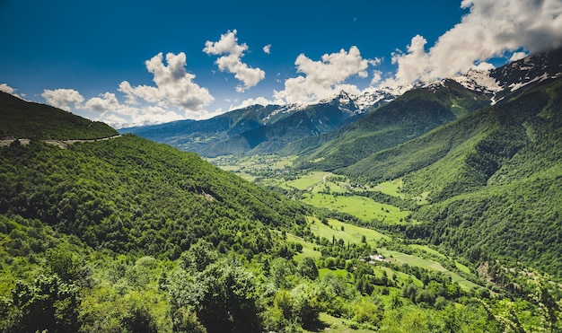 Panoramic summer landscape with green hill and mountain snow capped peak against blue cloudy sky. Svanetia region, Georgia. Main Caucasian ridge. Nature background. Holiday, hiking, travel, recreation