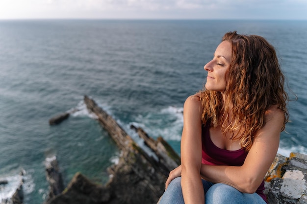 Panoramic top view of woman with eyes closed on holidays in Asturias. Horizontal view of cheerful woman isolated in blue sea in the background. Travel on holidays and people concept.