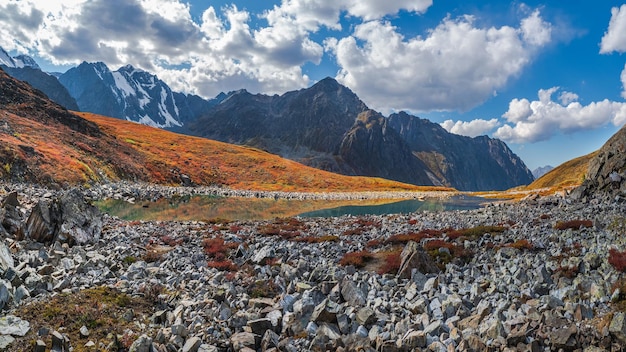 Panoramic view of the autumn mountain lake with reflection white clouds A clear blue mountain lake and a bright autumn stones floating in water