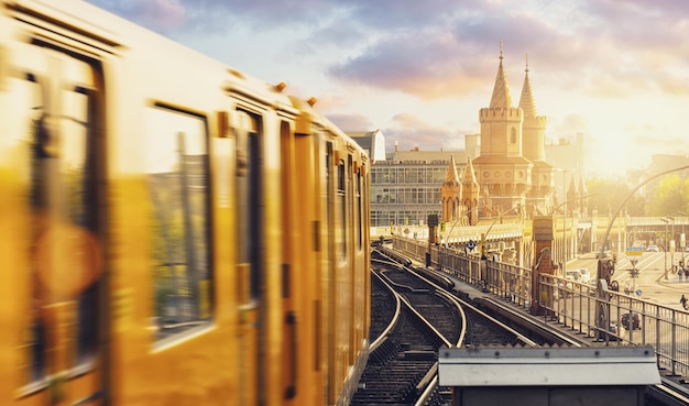 Panoramic view of Berliner UBahn with Oberbaum Bridge in the background in golden evening light at sunset with dramatic clouds Berlin FriedrichshainKreuzberg