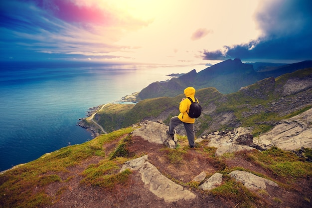 Panoramic view of fjord and fishing village. Man tourist standing on a cliff of rock. Beautiful mountain landscape. Nature Norway, Lofoten islands