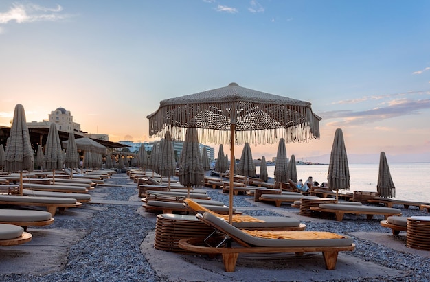 Panoramic view of Mediterranean Sea from beach with closed umbrellas and sunbeds against backdrop of colorful sunset of Rhodes Greece