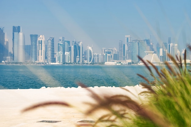 Panoramic view of modern skyline of Doha with green grass and beach foreground. Concept of healthy environment.