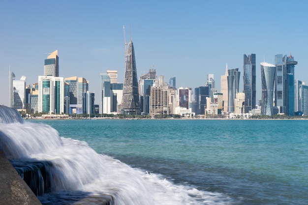 Panoramic view of modern skyline of Doha with small waterfall foreground. Qatar on sunny day.