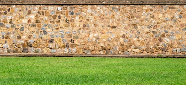 Panoramic view of the old vintage stone wall and green lawn at a garden as landscape design