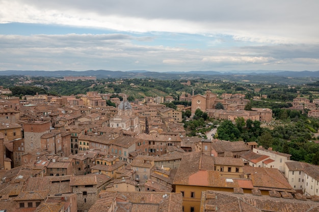 Panoramic view of Siena city with historic buildings and far away green fields from Torre del Mangia is a tower in city. Summer sunny day and dramatic blue sky