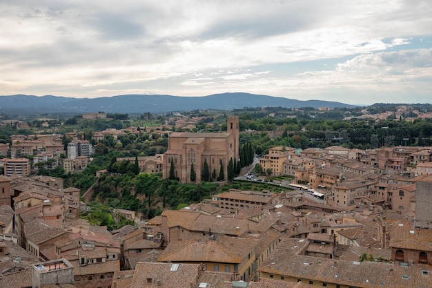 Panoramic view of Siena city with historic buildings and far away green fields from Torre del Mangia is a tower in city. Summer sunny day and dramatic blue sky