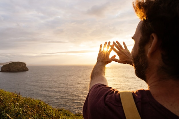 Panoramic view of unrecognizable man at sunset in a cliff. Horizontal view of backpacker traveling outdoors with the blue ocean on the background.