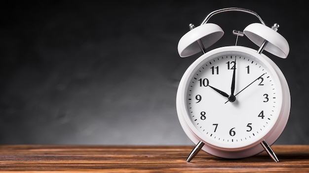 Panoramic view of white alarm clock on wooden desk against gray background