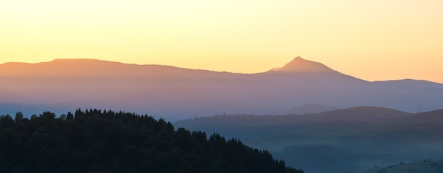 Panoramicl mountain landscape with hazy peaks and foggy wooded valley at sunset.