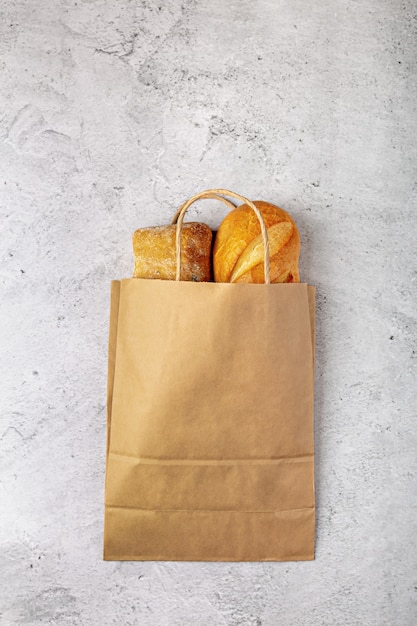 Paper bag from supermarket recyclable with baked loaves of bread flat lay on gray background with copy space