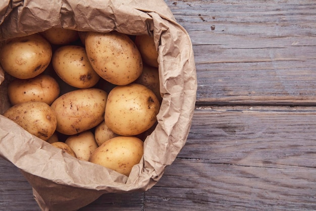 A paper bag full of fresh homegrown potatoes on a wooden background