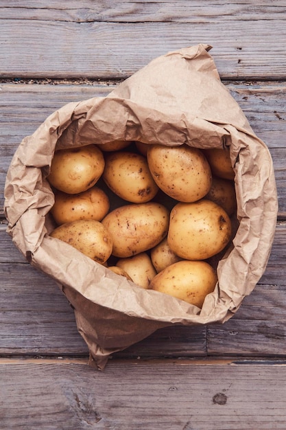 A paper bag full of fresh homegrown potatoes on a wooden background