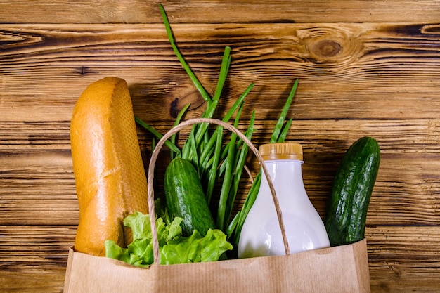 Paper bag with different food from grocery on a wooden table Supermarket shopping concept Top view