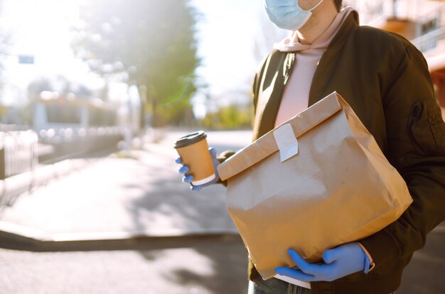 The paper bag with food and coffee in the hands of the courier in quarantine city. Delivery service under quarantine, disease outbreak, coronavirus covid-19 pandemic conditions.