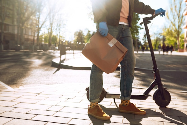 The paper bag with food and coffee in the hands of the courier in quarantine city. Delivery service under quarantine, disease outbreak, coronavirus covid-19 pandemic conditions.