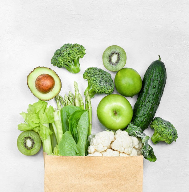 Paper bag with green vegetables and fruits on a gray concrete background