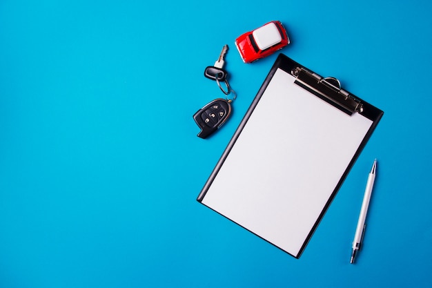 Paper blank with toy red car and keys on a blue background. Technical inspection or car credit 