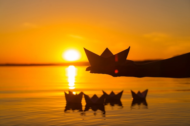 Paper boat is on a palm of boy. four paper origami which float in the river at sunset