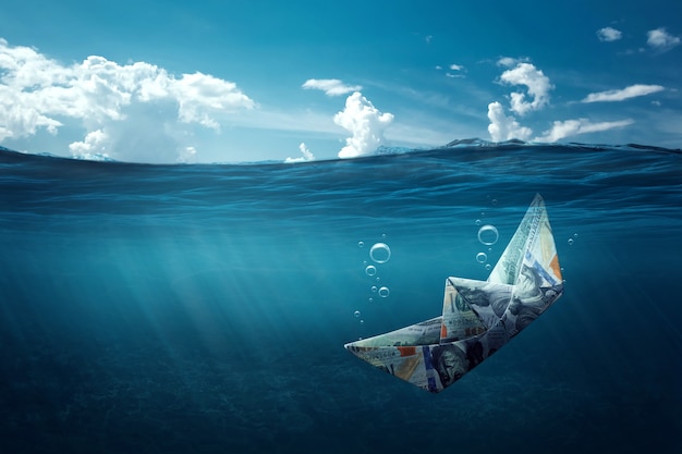 A paper boat made of money sinks into the sea under water. Financial crisis concept, debts, paying bills, mortgage, bankruptcy.