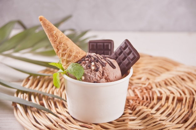 Paper bowl of chocolate ice cream with small waffle cone and chocolate