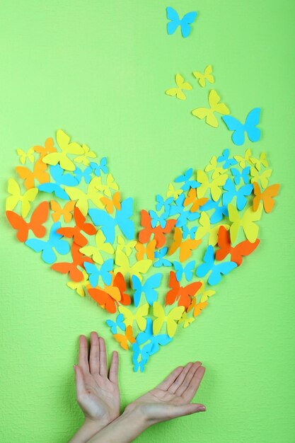 Paper butterflies on hands on green wall background