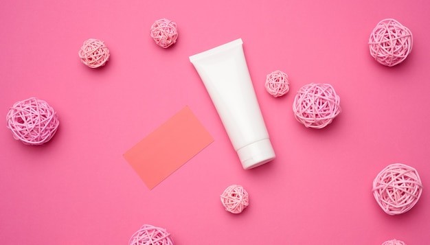 Paper card and empty white plastic tubes for cosmetics on a pink background. Packaging for cream, gel, serum, advertising and product promotion, mock up