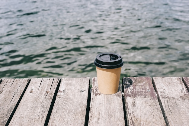 Paper coffee cup on wood near sea