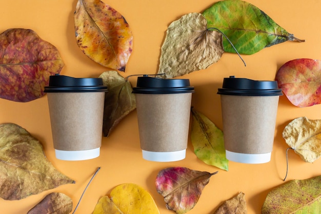 Paper coffee cups with lids in autumn leaves with orange background