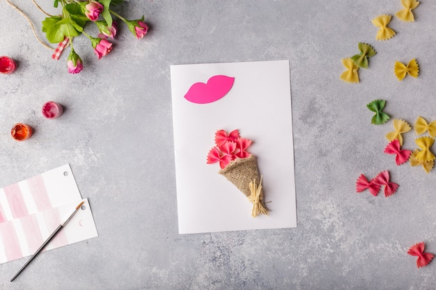 Paper crafts for mother day, 8 march or birthday. Small child doing a bouquet of flowers out of colored paper and colored pasta.