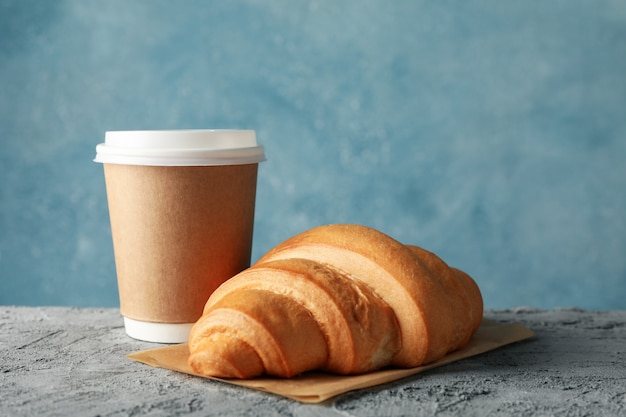 Paper cup of coffee and croissant on grey table, space for text