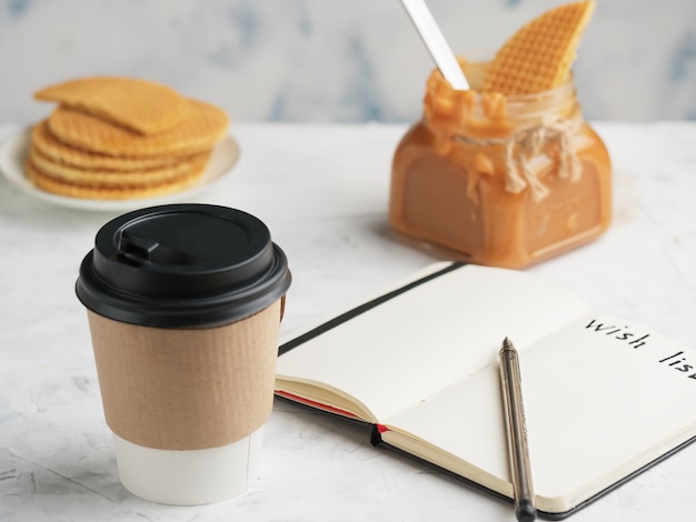 Paper cup with coffee or hot drink on the table. Notepad with a wish sheet.