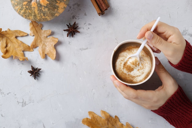 Paper cup with delicious pumpkin latte with spices in female hands on a gray table