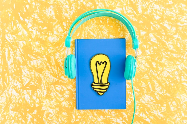 Paper cut out yellow light bulb on closed notebook with headphone on textured background