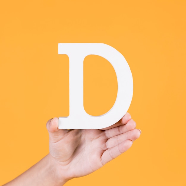 Paper cutout of letter d hold by human hand on yellow backdrop