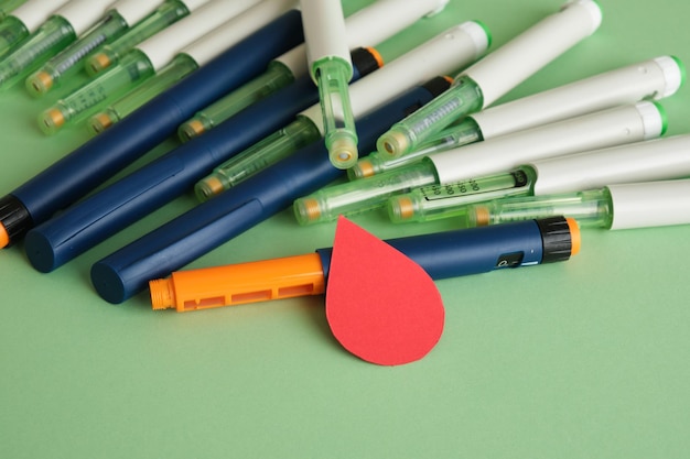 A paper drop of blood and a lot of syringe pens with insulin on a green background